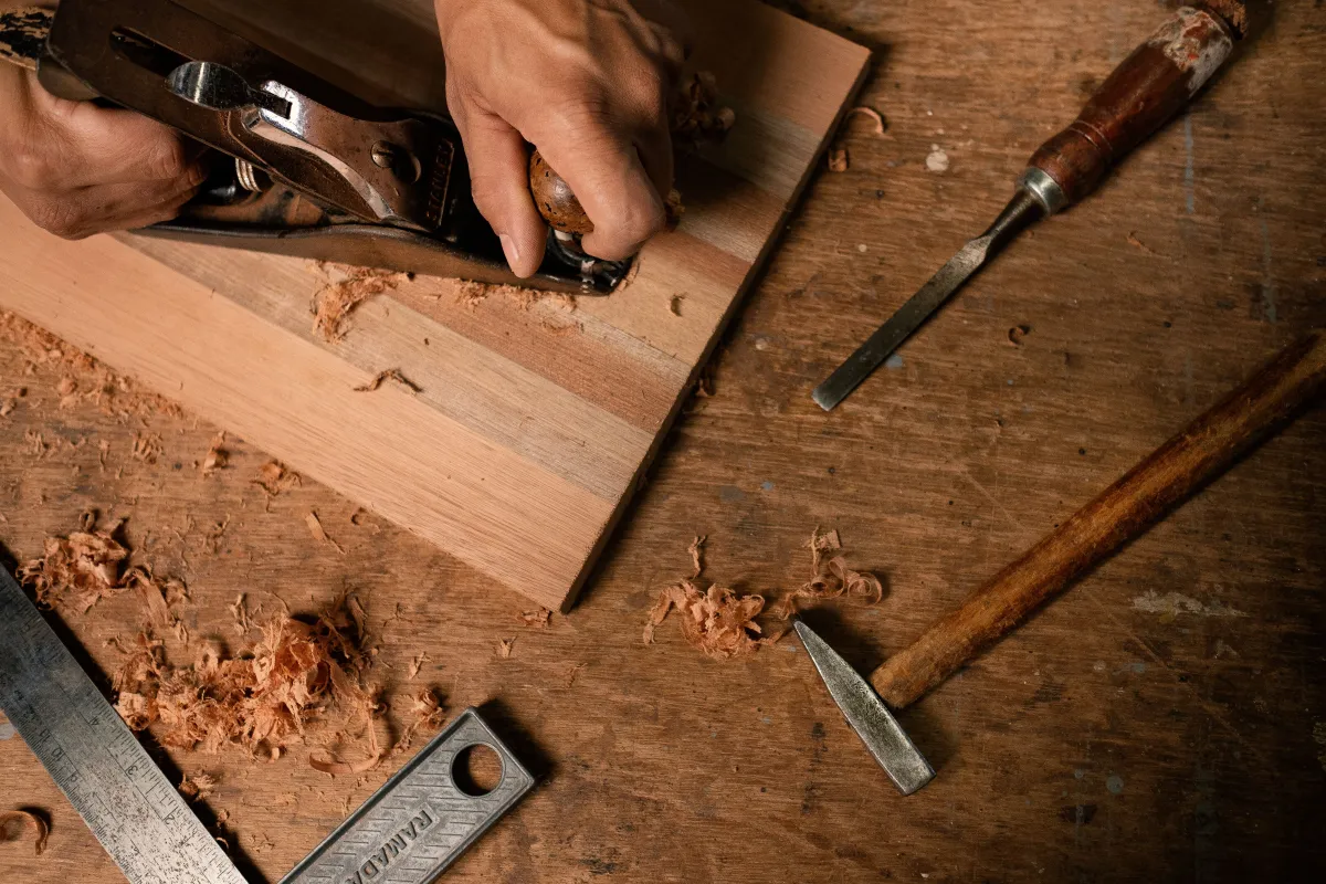 Essential beginner woodworking tools including tape measure, square, cordless drill, and sander laid out on a workbench